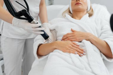 Genç bir kız güzellik salonunda ellerinin derisi için karbon soyuluyor. Lazer darbeleri deriyi temizler. Donanım kozmetolojisi. Fototermoliz süreci, deriyi ısıtır..