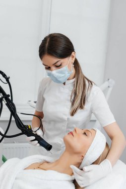 Genç bir kız güzellik salonunda boynun derisi için karbon soyuyorlar. Lazer darbeleri deriyi temizler. Donanım kozmetolojisi. Fototermoliz süreci, deriyi ısıtır..