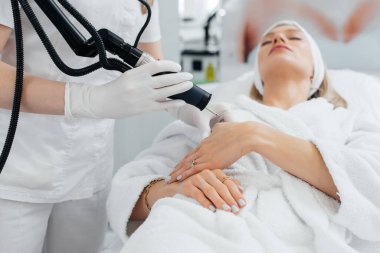 Genç bir kız güzellik salonunda ellerinin derisi için karbon soyuluyor. Lazer darbeleri deriyi temizler. Donanım kozmetolojisi. Fototermoliz süreci, deriyi ısıtır..