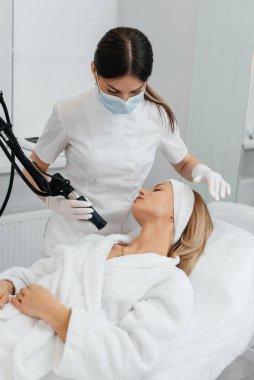 Genç bir kız güzellik salonunda boynun derisi için karbon soyuyorlar. Lazer darbeleri deriyi temizler. Donanım kozmetolojisi. Fototermoliz süreci, deriyi ısıtır..