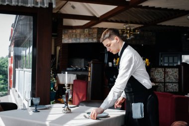 Şık üniformalı genç bir erkek garson güzel bir gurme restoranında masaya servis yapmakla meşgul. Üst düzey bir restoran. Restorandaki masa servisi..