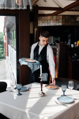 Şık üniformalı genç bir erkek garson güzel bir gurme restoranında masaya servis yapmakla meşgul. Üst düzey bir restoran. Restorandaki masa servisi..