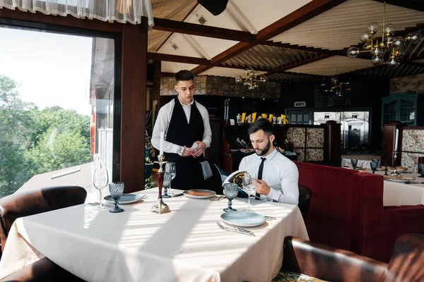一位年轻的商人在一家高档餐厅里检查菜单 并向一位穿着时髦围裙的年轻侍者下订单 客户服务 餐厅的餐桌服务 — 图库照片
