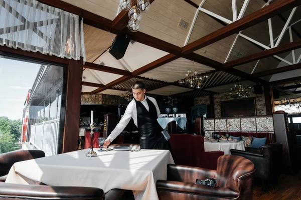 一位穿着时髦制服的年轻男服务员在一家漂亮的美食家餐厅里为餐桌服务 一个高级餐厅 餐厅的餐桌服务 — 图库照片