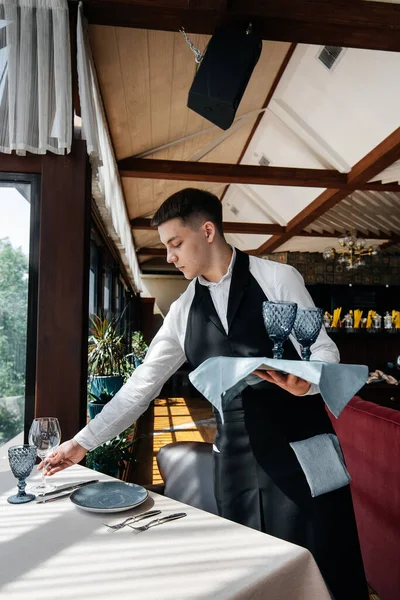 スタイリッシュな制服を着た若い男性ウエイターが美しいグルメレストランでテーブルを提供しています 高級レストランです レストランでのテーブルサービス — ストック写真