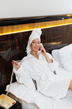 Beyaz önlüklü güzel bir kız otel odasında telefonla konuşuyor. Dinlen ve seyahat et. Otel eğlencesi ve turizm..