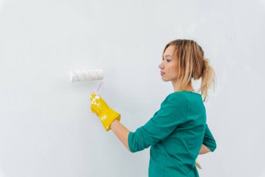 Genç bir kız, yeni bir dairede tamirat ve beyaz bir duvar boyuyor. Evin tadilatı ve yeni bir daire. Yeni ev ve istenen bir ipotek..