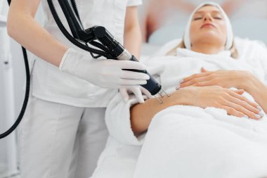 Genç bir kız güzellik salonunda ellerinin derisi için karbon soyuluyor. Lazer darbeleri deriyi temizler. Donanım kozmetolojisi. Fototermoliz süreci, deriyi ısıtır..