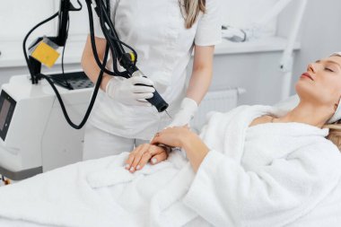 Genç bir kız güzellik salonunda ellerinin derisi için karbon soyuluyor. Lazer darbeleri deriyi temizler. Donanım kozmetolojisi. Fototermoliz süreci, deriyi ısıtır..