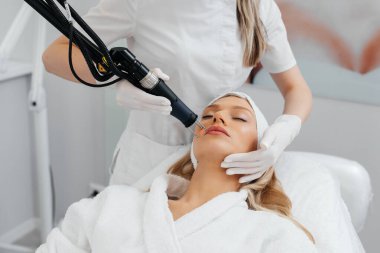 Genç bir kız güzellik salonunda yüzünün derisi için kömür soyuyordu. Lazer darbeleri deriyi temizler. Donanım kozmetolojisi. Fototermoliz süreci, deriyi ısıtır..