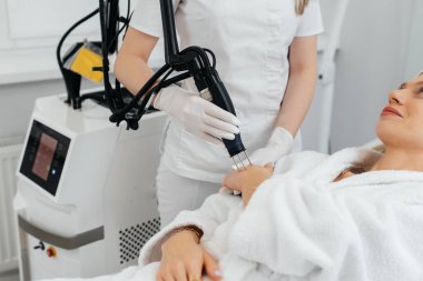 Genç bir kız güzellik salonunda ellerinin derisi için karbon soyuluyor. Lazer darbeleri deriyi temizler. Donanım kozmetolojisi. Fototermoliz süreci, deriyi ısıtır..