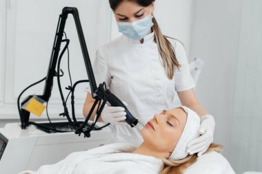 Genç bir kız güzellik salonunda yüzünün derisi için kömür soyuyordu. Lazer darbeleri deriyi temizler. Donanım kozmetolojisi. Fototermoliz süreci, deriyi ısıtır..