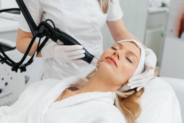 Genç bir kız güzellik salonunda yüzünün derisi için kömür soyuyordu. Lazer darbeleri deriyi temizler. Donanım kozmetolojisi. Fototermoliz süreci, deriyi ısıtır..