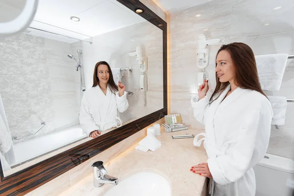 Genç güzel bir kız güzel beyaz bir banyoda dişlerini fırçalıyor. Otelde taze bir günaydın. Dinlen ve seyahat et. Otel eğlencesi ve turizm..