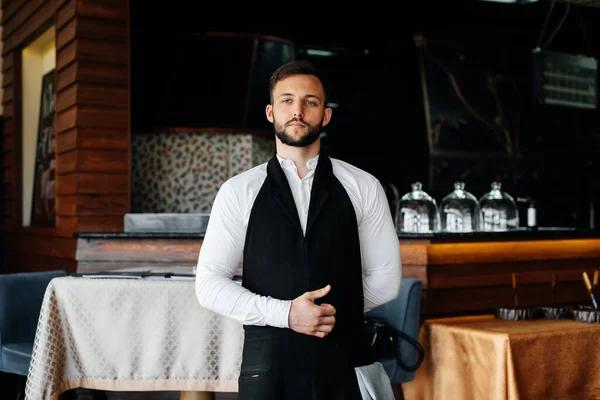 A young waiter with a beard puts on an apron and prepares for a working day in a fine restaurant.