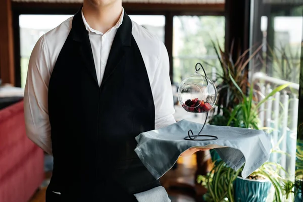 Şık bir üniforma içindeki genç bir garson, güzel bir restoranın yakın çekiminde masanın yanındaki tepside nefis bir tabakla duruyor. Restoran faaliyetleri, en üst düzeyde..