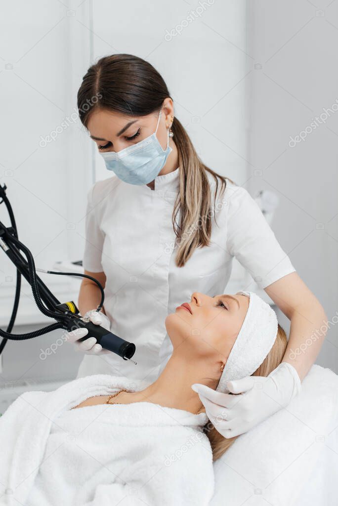 A young girl gets a carbon peeling for the skin of the neck in a beauty salon. Laser pulses cleanse the skin. Hardware cosmetology. The process of photothermolysis, warming the skin.