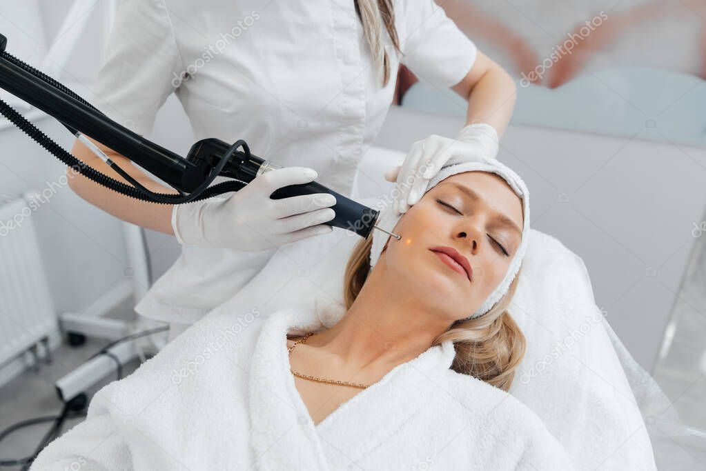 A young girl gets a charcoal peeling for the skin of the face in a beauty salon. Laser pulses cleanse the skin. Hardware cosmetology. The process of photothermolysis, warming the skin.
