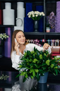 Genç bir çiçekçi kadın, güzel bir çiçek buketi yapımı için telefonla siparişi kabul ediyor. Çiçekçilik ve çiçekçide kova yapmak. Küçük işletme.