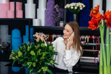 Genç bir çiçekçi kadın, güzel bir çiçek buketi yapımı için telefonla siparişi kabul ediyor. Çiçekçilik ve çiçekçide kova yapmak. Küçük işletme.