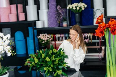 Genç bir çiçekçi kadın, güzel bir çiçek buketi yapımı için telefonla siparişi kabul ediyor. Çiçekçilik ve çiçekçide kova yapmak. Küçük işletme.
