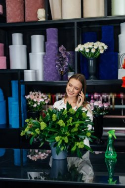 Genç bir çiçekçi kadın, güzel bir çiçek buketi yapımı için telefonla siparişi kabul ediyor. Çiçekçilik ve çiçekçide kova yapmak. Küçük işletme.