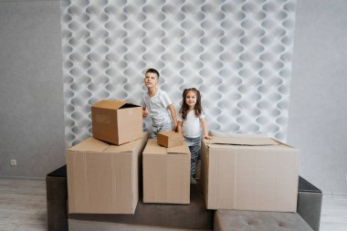 Erkek ve kız kardeş kanepedeki karton kutuların arka planına karşı yeni bir daireye taşınıp eğleniyorlar. Gayrimenkul alımı. Ev partisi, teslimat..