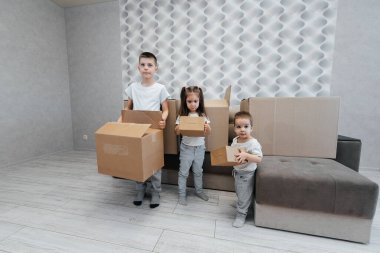Erkek ve kız kardeşler karton kutuların ve kanepenin arka planında yeni bir daireye taşınıp eğleniyorlar. Gayrimenkul alımı. Ev partisi, teslimat..