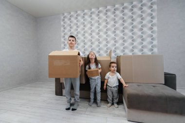 Erkek ve kız kardeşler karton kutuların ve kanepenin arka planında yeni bir daireye taşınıp eğleniyorlar. Gayrimenkul alımı. Ev partisi, teslimat..