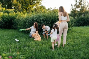 Gün batımında bir grup yetişkin ve çocuk parkta çöp toplamakla meşgul. Çevresel bakım, atık geri dönüşümü. Çöp ayıklama.