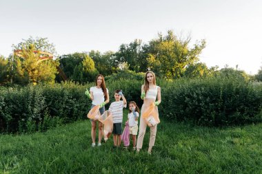 Gün batımında bir grup yetişkin ve çocuk parkta çöp toplamakla meşgul. Çevresel bakım, atık geri dönüşümü. Çöp ayıklama.