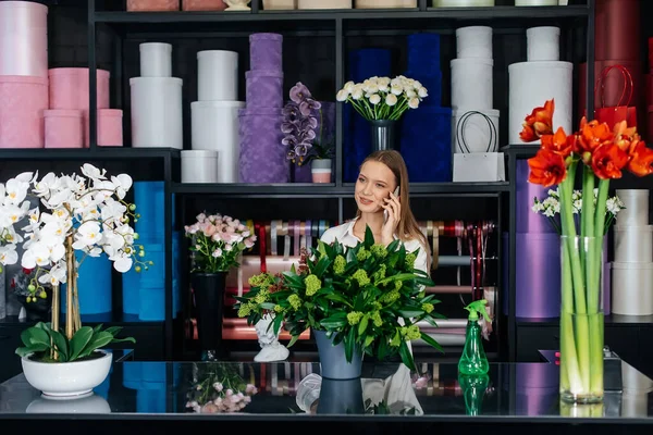 Genç bir çiçekçi kadın, güzel bir çiçek buketi yapımı için telefonla siparişi kabul ediyor. Çiçekçilik ve çiçekçide kova yapmak. Küçük işletme.
