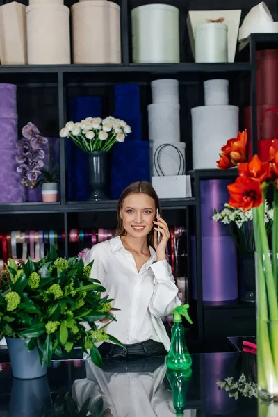 Genç bir çiçekçi kadın, güzel bir çiçek buketi yapımı için telefonla siparişi kabul ediyor. Çiçekçilik ve çiçekçide kova yapmak. Küçük işletme.
