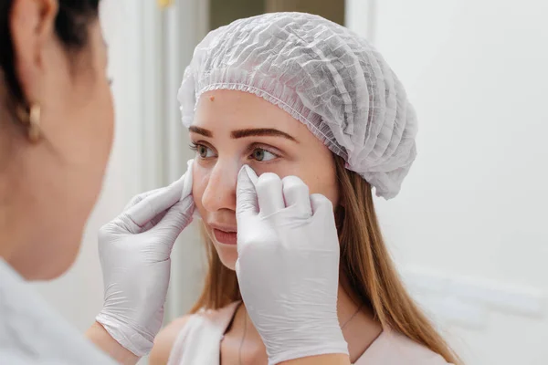 美容师在给一个年轻漂亮的女孩填入鼻腔沟和进行眼部周围的中间治疗后 擦拭病人的脸 现代美容学 图库图片