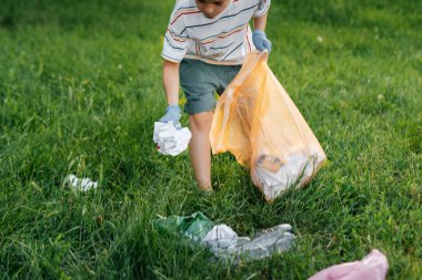 Gün batımında yedi yaşında bir çocuk parkta çöp toplamakla meşgul. Çevre bakımı, geri dönüşüm.