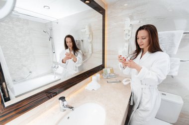 Güzel beyaz bir banyoda genç ve güzel bir kız telefonda konuşuyor. Otelde taze bir günaydın. Dinlen ve seyahat et. Otel eğlencesi ve turizm..