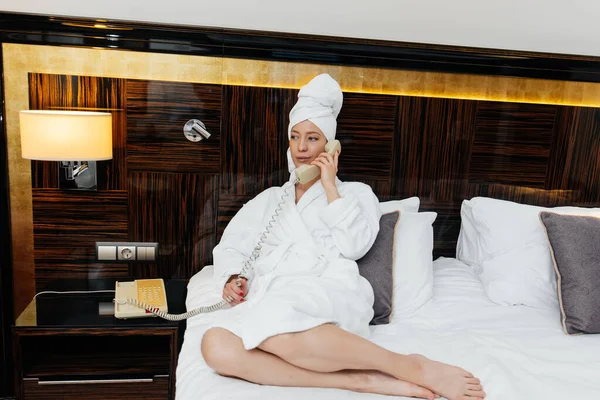 Beyaz önlüklü güzel bir kız otel odasında telefonla konuşuyor. Dinlen ve seyahat et. Otel eğlencesi ve turizm..