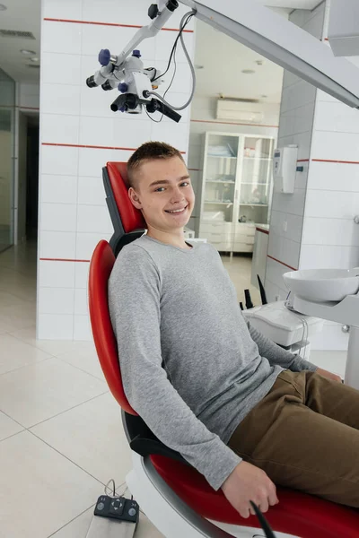 Młody Mężczyzna Siedzi Czerwonym Krześle Dentystycznym Uśmiecha Się Nowoczesnej Białej — Zdjęcie stockowe