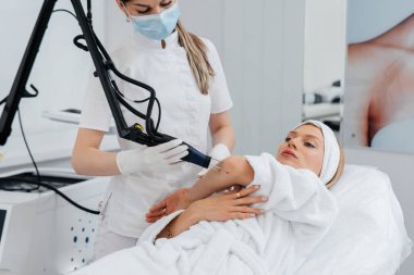 Genç bir kız güzellik salonunda ellerinin derisi için karbon soyuluyor. Lazer darbeleri deriyi temizler. Donanım kozmetolojisi. Fototermoliz süreci, deriyi ısıtır..
