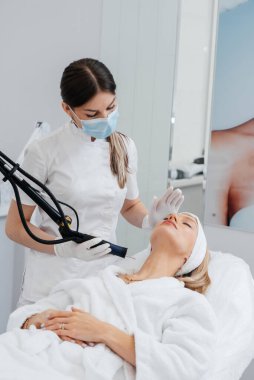 Genç bir kız güzellik salonunda boynun derisi için karbon soyuyorlar. Lazer darbeleri deriyi temizler. Donanım kozmetolojisi. Fototermoliz süreci, deriyi ısıtır..