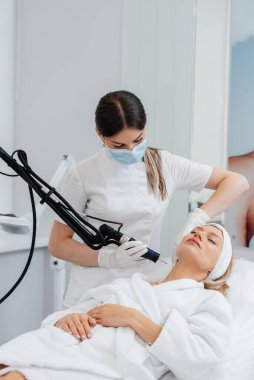 Genç bir kız güzellik salonunda boynun derisi için karbon soyuyorlar. Lazer darbeleri deriyi temizler. Donanım kozmetolojisi. Fototermoliz süreci, deriyi ısıtır..