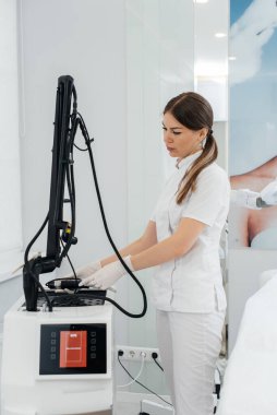 Bir kozmetolog, güzellik salonunda lazerli modern bir cihaz kuruyor. Lazer darbeleri deriyi temizler. Donanım kozmetolojisi. Fototermoliz süreci, deriyi ısıtır..