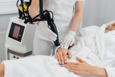 Genç bir kız güzellik salonunda ellerinin derisi için karbon soyuluyor. Lazer darbeleri deriyi temizler. Donanım kozmetolojisi. Fototermoliz süreci, deriyi ısıtır..