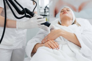 Genç bir kız güzellik salonunda ellerinin derisi için karbon soyuluyor. Lazer darbeleri deriyi temizler. Donanım kozmetolojisi. Fototermoliz süreci, deriyi ısıtır..