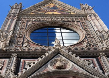 Siena Toskana 'nın ünlü katedralinin cephesinde gökyüzünü yansıtan büyük yuvarlak bir pencere. Güzel bir bahar günü, mavi bir gökyüzü ve birkaç bulutla.