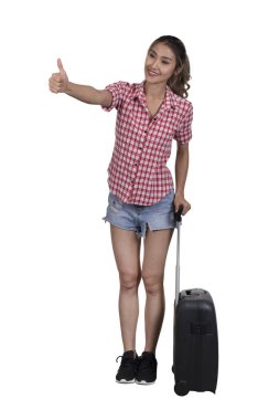 Kırmızı ekose gömlek ve kısa kot giyen bayan turist yolculukta bavullarıyla baş parmağını gösteriyor..