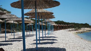 Sahil şemsiyeleri, İyon Denizi 'nin çakıl taşı kumsalında dizilmişti..                   