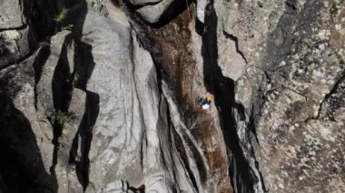 Tanımlanamayan iki insan canlanırken ipten iniyor. İnsanlar dar nehir yatakları, şelaleler ve kanyonlardan iple inme ve geçme pratiği yapıyor. Canyoning, bakir doğada yüksek adrenalin içeren bir spordur.