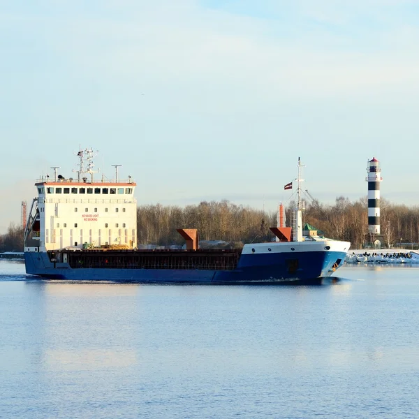 Cargo ship leaving port with lighthouse at the background — Stock Photo, Image