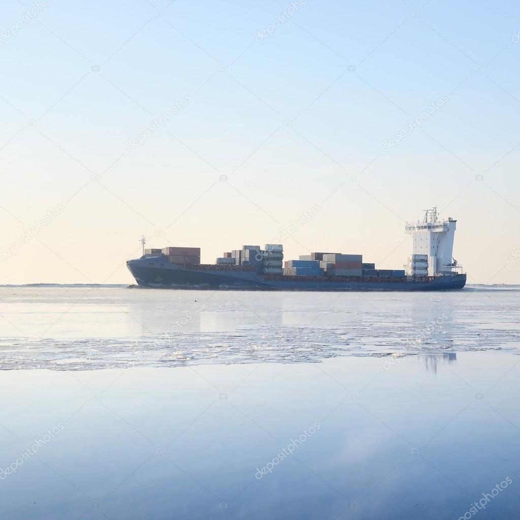 Cargo container ship sailing in still frozen winter sea